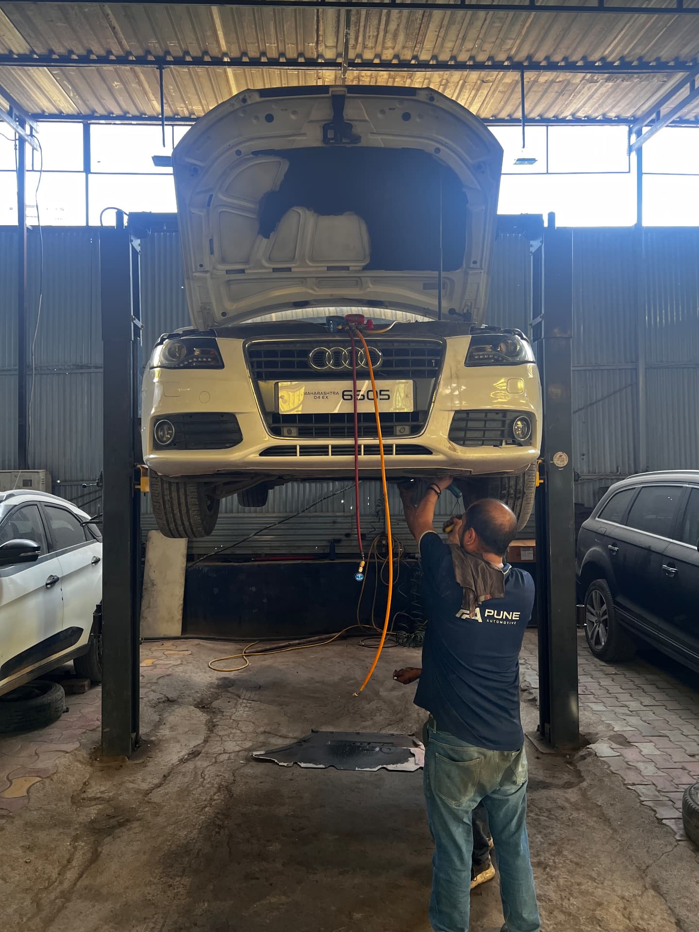 Pune Automotive technician in branded uniform working underneath an Audi raised on a lift